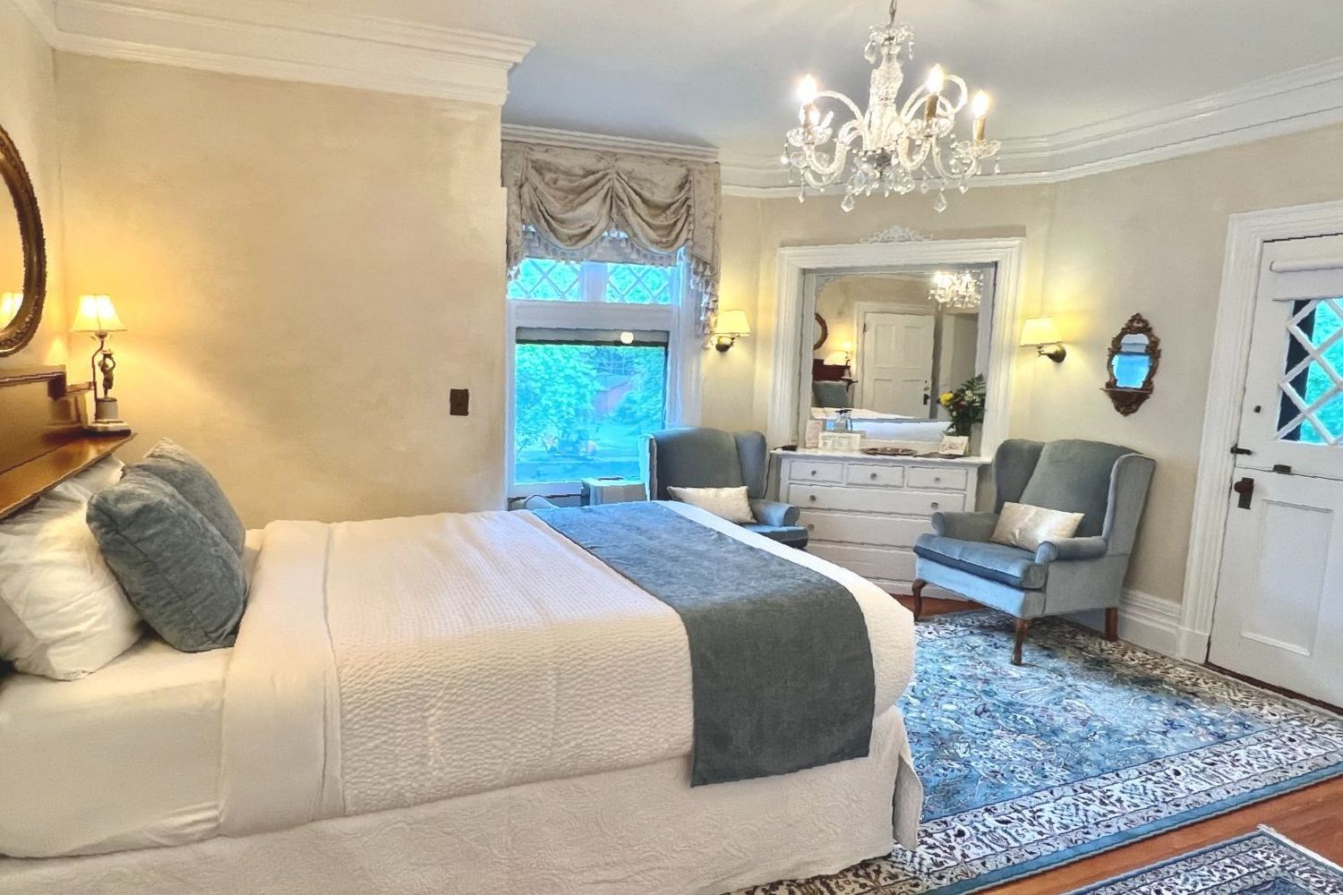 A bedroom with a king size bed , chairs , dresser and mirror.