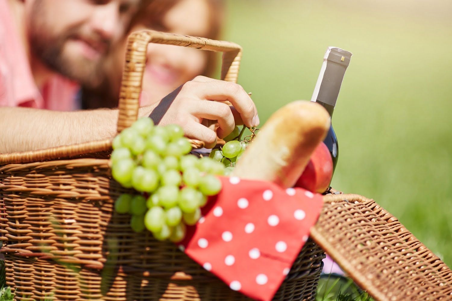 A couple with a picnic basket with grapes, bread and a bottle of wine.