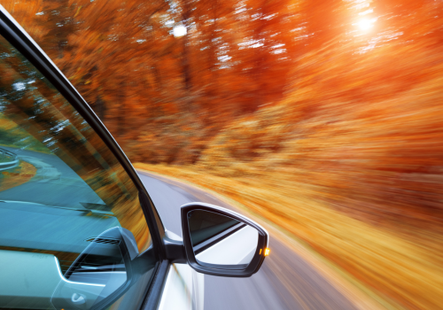 Car speeding along a curving road through blurred orange autumn trees