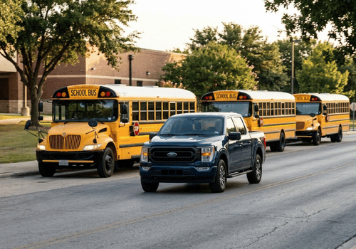 Blue Ford F-150 driving through a school zone alongside school buses