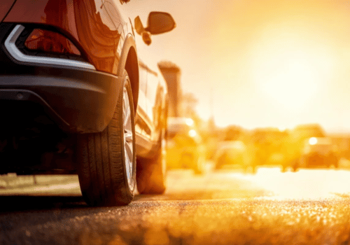 Close-up of a car tire on a wet road at sunset, with warm orange sunlight reflecting off the pavement
