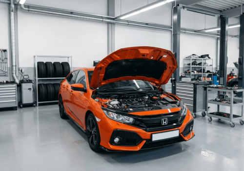 Orange Honda Civic hatchback inside a clean, modern auto repair shop with the hood open