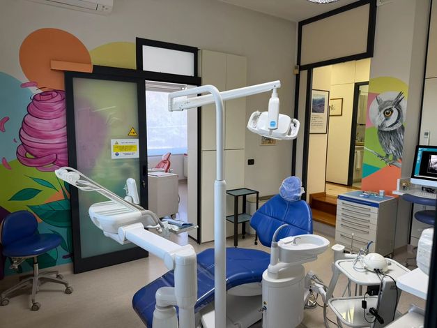 Studio odontoiatrico con poltrona blu, lampada scialitica e attrezzature dentistiche in uno spazio di lavoro colorato