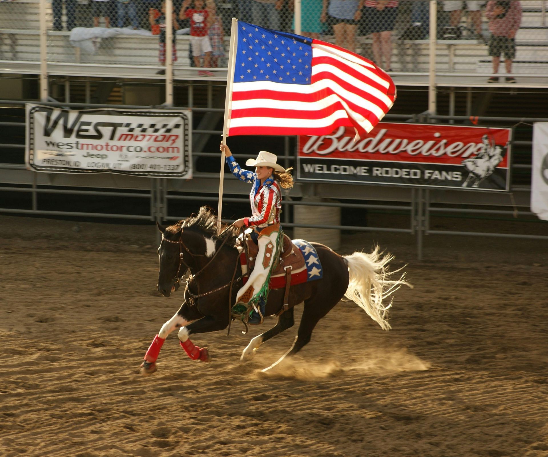Woman on horseback waving American flag in rodeo arena.