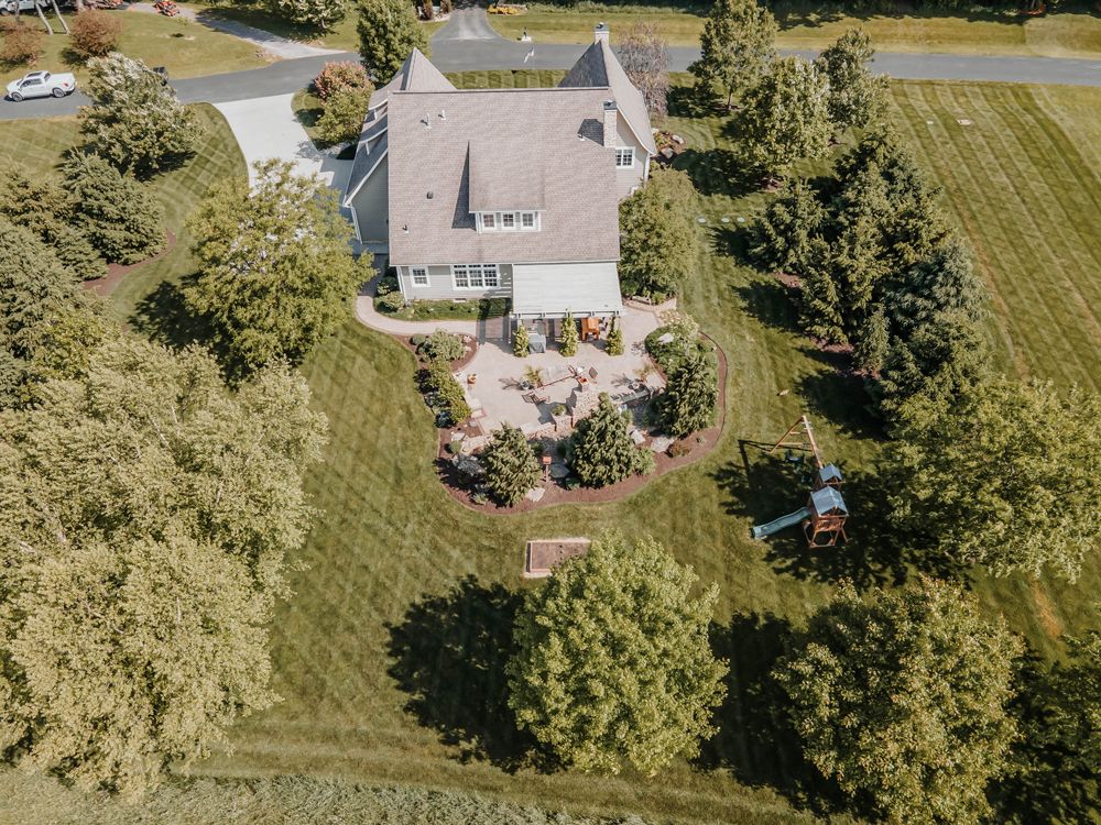 Aerial view of a two-story house with a stone patio and manicured lawn surrounded by trees.