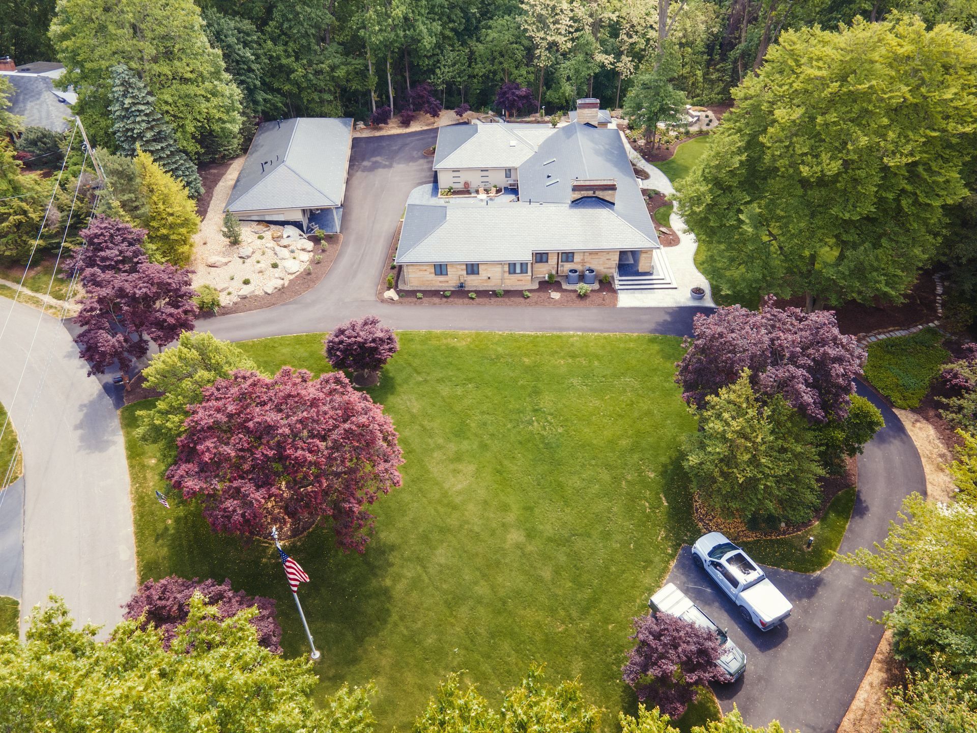 Aerial view of a house with a large green lawn with red-leafed trees. 