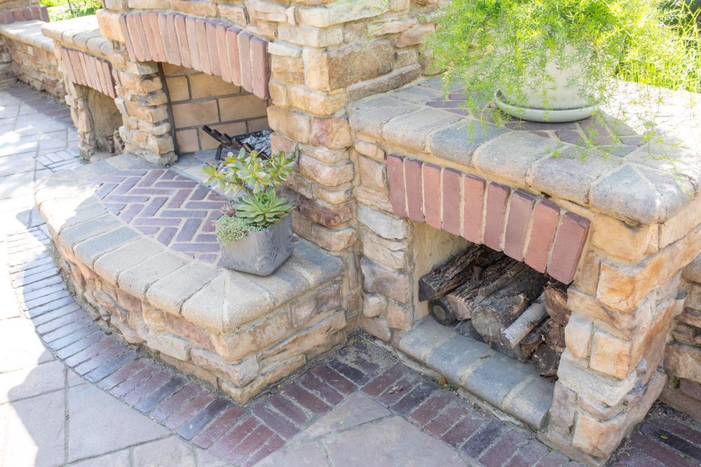 Outdoor stone fireplace with brick accents; firewood is stacked inside, and potted plants sit on top.