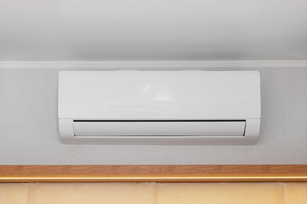 Wall-mounted white air conditioner above a wooden trim on a light gray wall