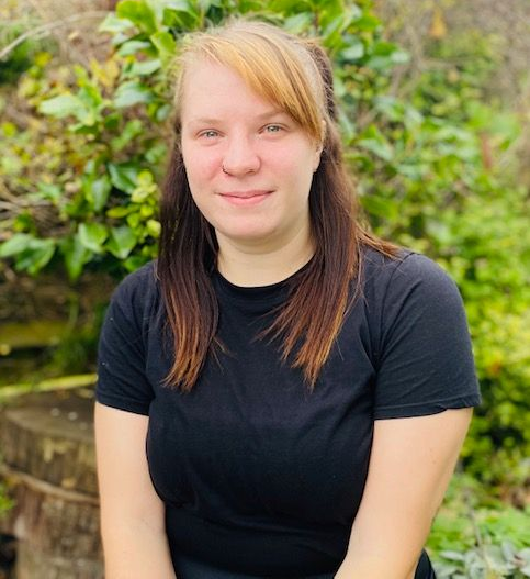 Woman with blonde bangs, brown hair, and black shirt smiling outside.