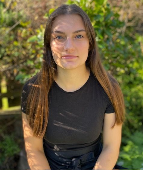 A woman in a black shirt is standing in front of a tree.