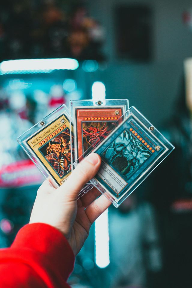 Hand holding three colorful trading cards against a blurred neon-lit background