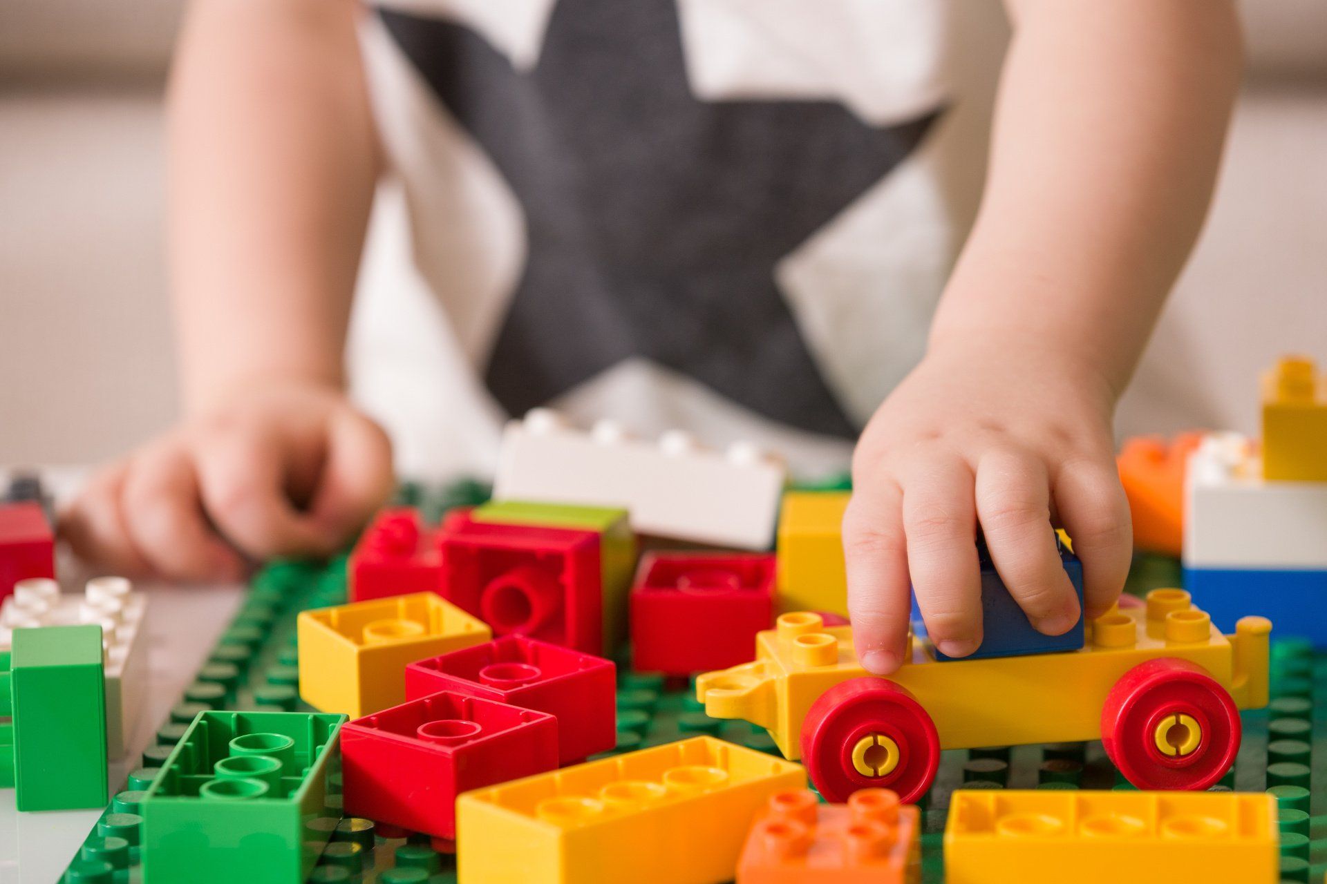 Child's hands playing with colorful building blocks on a green baseplate.