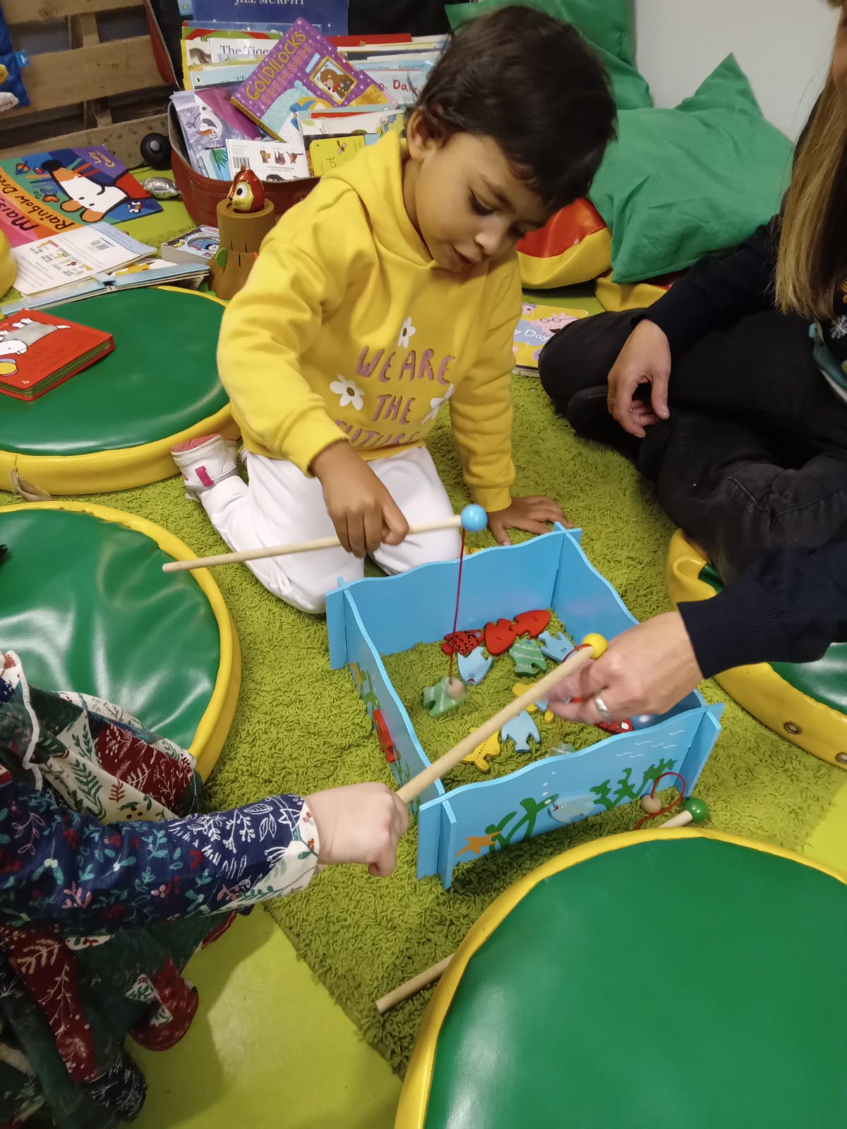 Child playing fishing game with two adults on green mats.