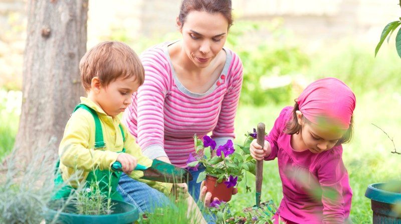 Woman and two children gardening, planting flowers in pots outside.