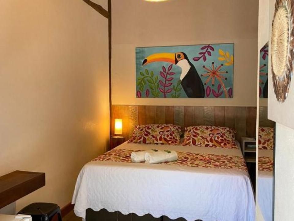 Um quarto de hotel com uma cama queen-size com roupa de cama floral, um quadro de tucano na parede e uma mesa de cabeceira com um abajur.