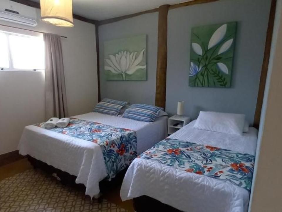 Um quarto de hotel com duas camas, caminhos de mesa florais, roupa de cama branca e duas pinturas com temas da natureza em paredes cinza-claro.