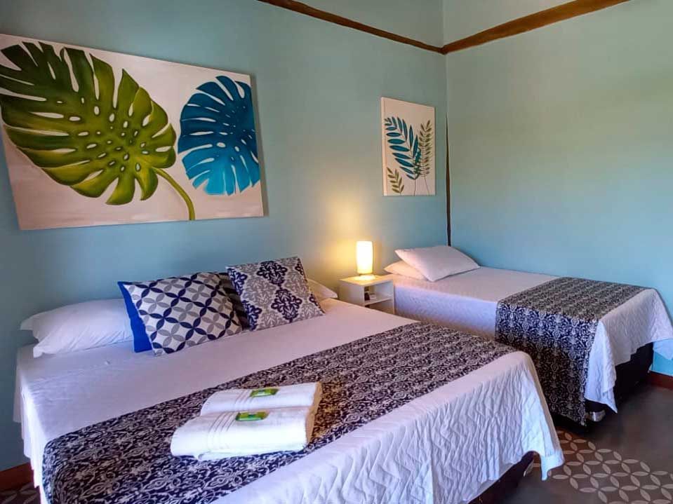 Um quarto de hotel com duas camas: uma cama de casal com peseiras estampadas e uma cama de solteiro, ambas com paredes azuis e decoração com folhas.