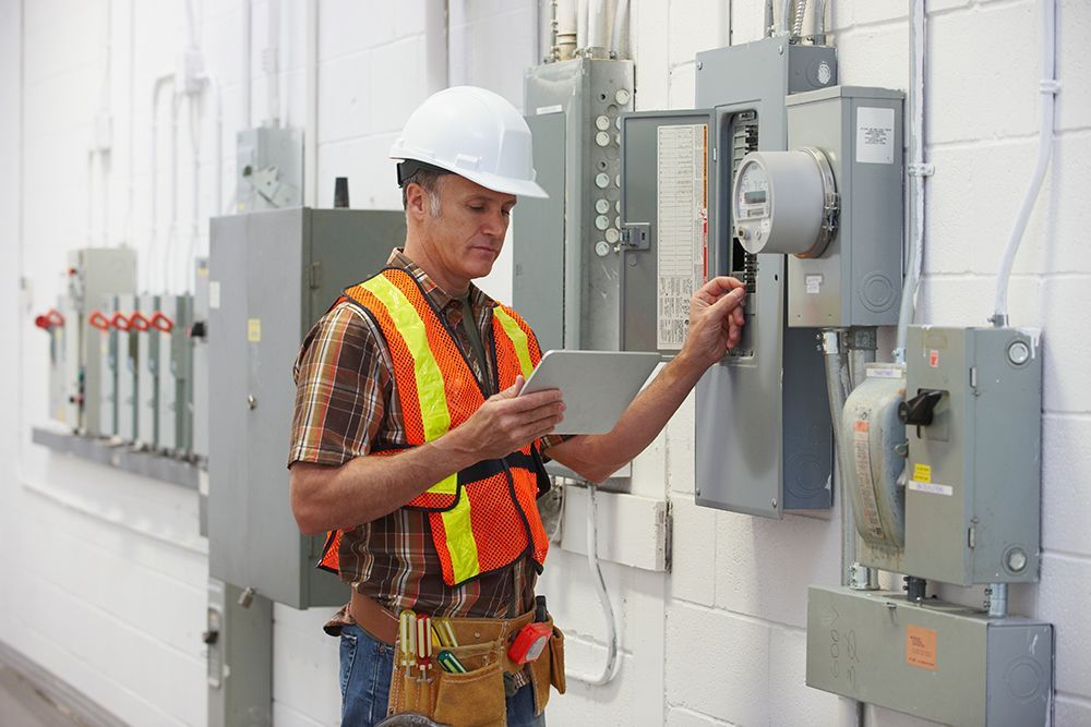 A man in a hard hat and safety vest is looking at a tablet.