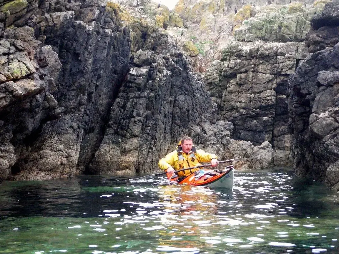 Paddle Northern Ireland | A man in a yellow jacket is riding a kayak in the water.