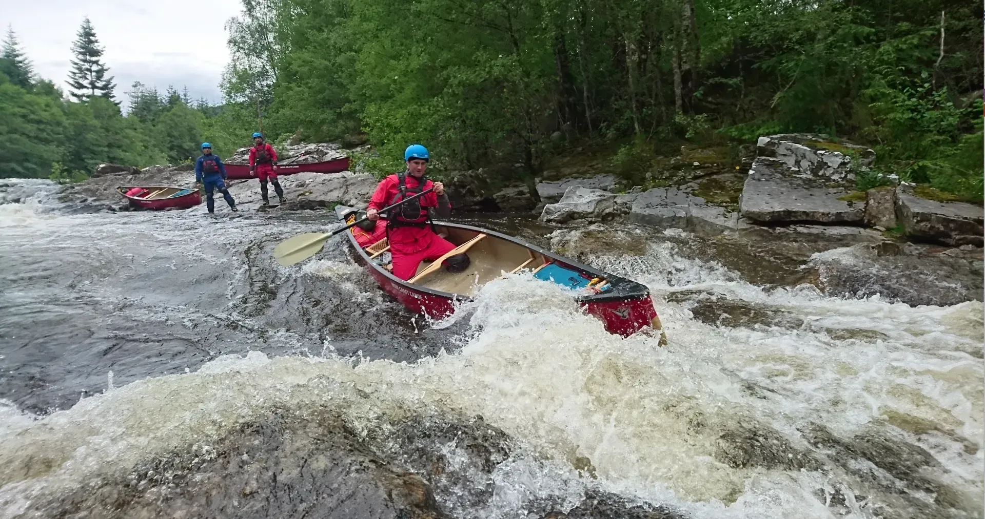A man in a red canoe is going through a river.