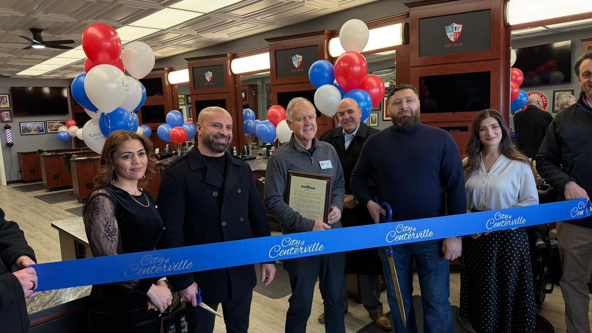 Group stands at a ribbon-cutting ceremony indoors with red, white, and blue balloons.