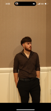A man in dark clothing stands against a beige wall, looking to the side.