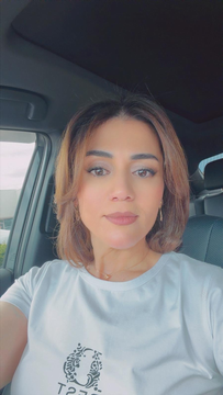 Person sitting in a car, wearing a white T-shirt, looking at the camera.