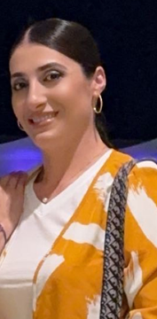 Woman smiling in a white and yellow patterned top with gold hoop earrings and a shoulder bag at night