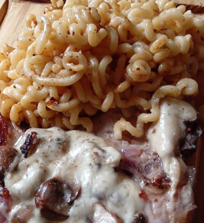Pasta con salsa blanca cremosa y carne dorada en un plato.