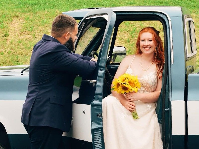 A bride and groom are sitting in the back of a truck.