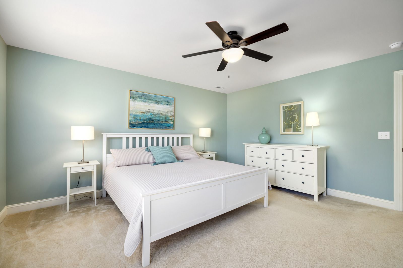 Bedroom with white bed, dresser, and nightstands; light blue walls, beige carpet.