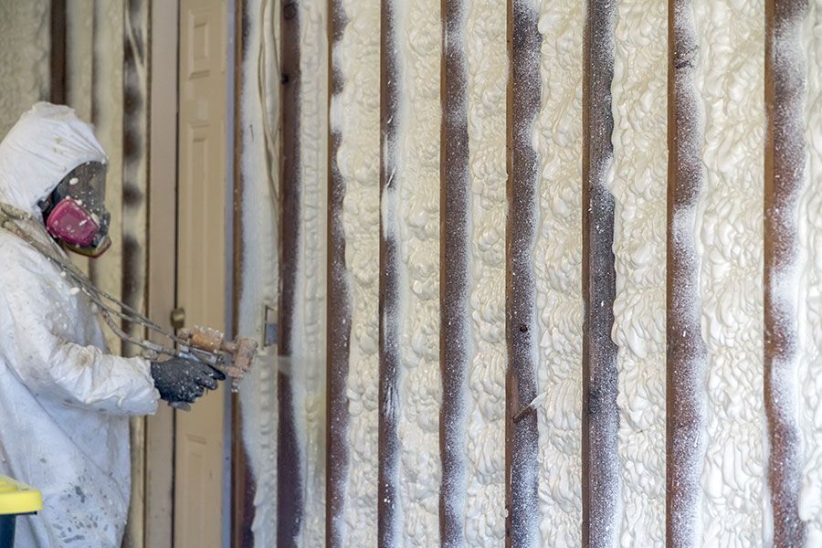 Person in protective suit spraying foam insulation onto wooden wall.