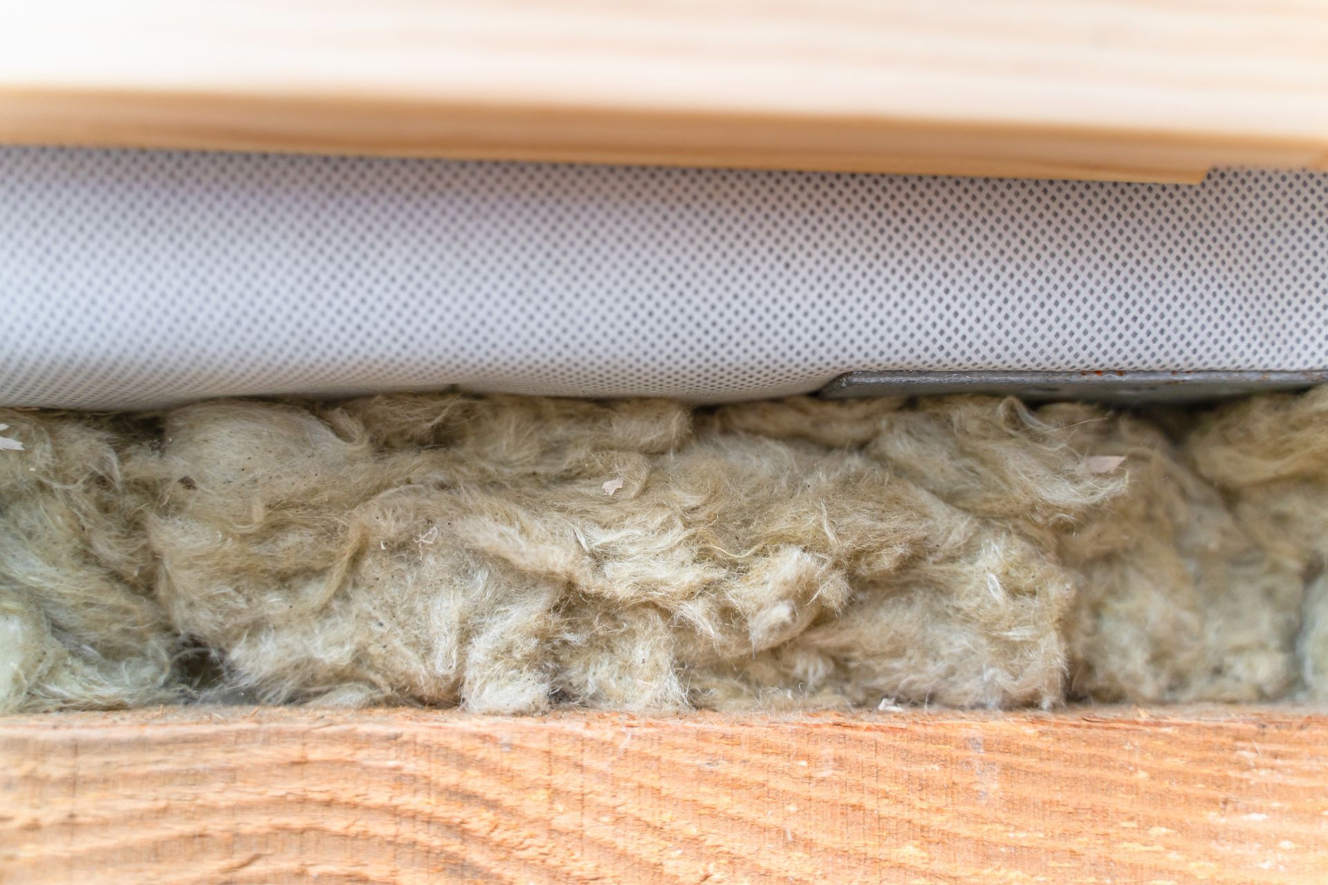 Insulation material (likely fiberglass) between wooden beams, covered with a white mesh fabric.
