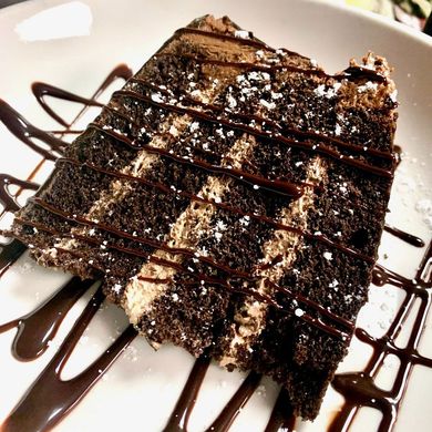 a piece of chocolate cake with chocolate sauce and powdered sugar on a white plate
