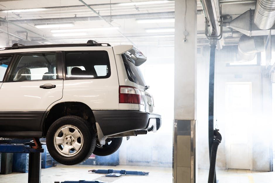 Silver SUV on a hydraulic lift in an auto repair shop, with bright light and a mechanic nearby