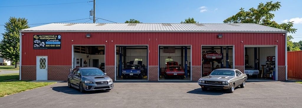 Red auto repair shop with red siding and three garage bays, two cars parked in front.