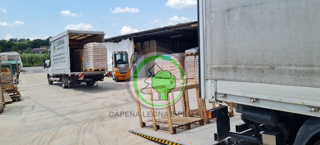 In un magazzino industriale all'aperto, un carrello elevatore carica dei pallet su un camion, insieme a materiali edili impilati.