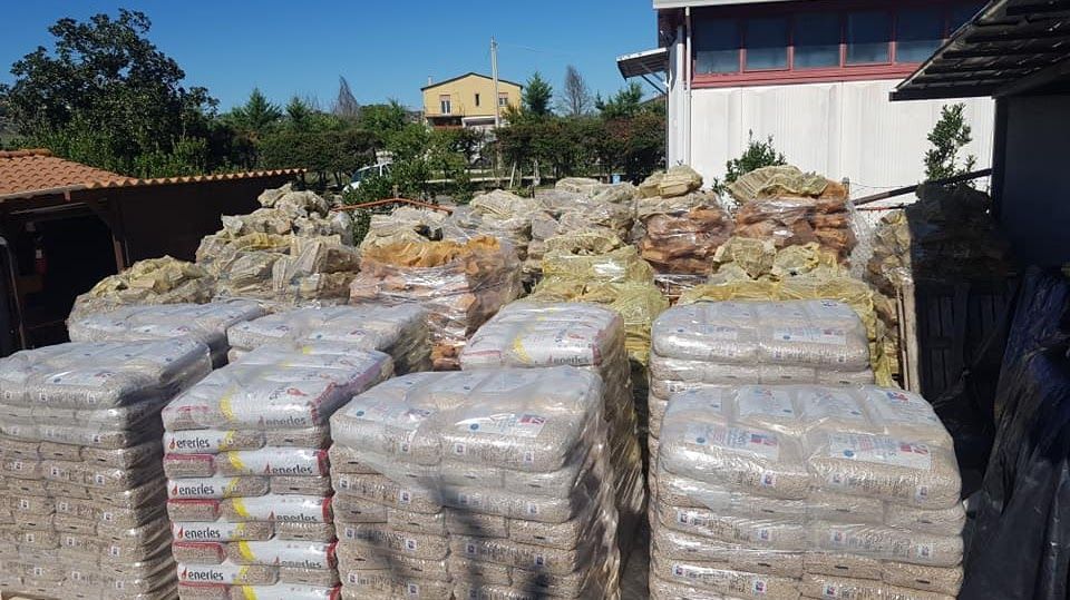 Pallet di materiali insacchettati e cumuli di pietre sfuse accatastati in un cortile all'aperto in una giornata di sole.