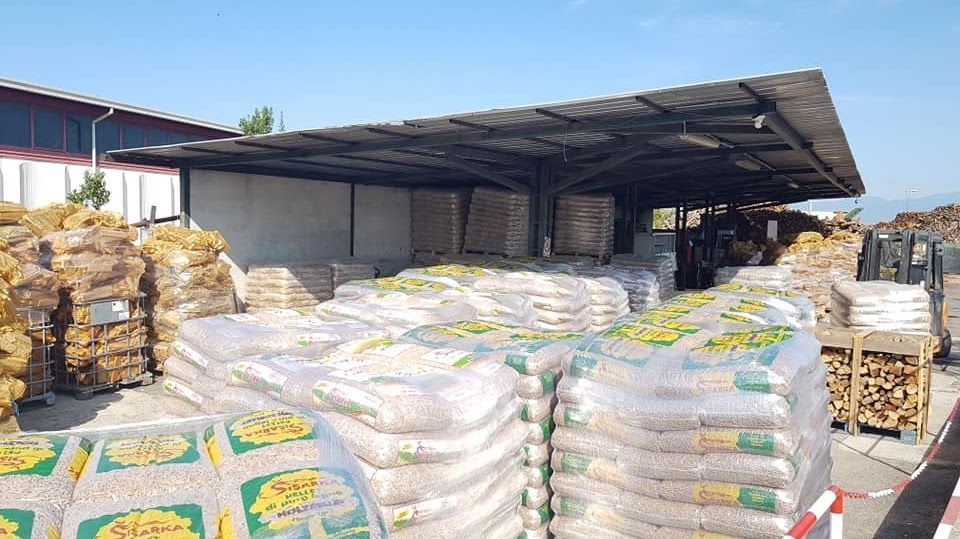 Pallet impilati di pellet di legno in sacchi sotto una struttura di stoccaggio esterna coperta presso un deposito.