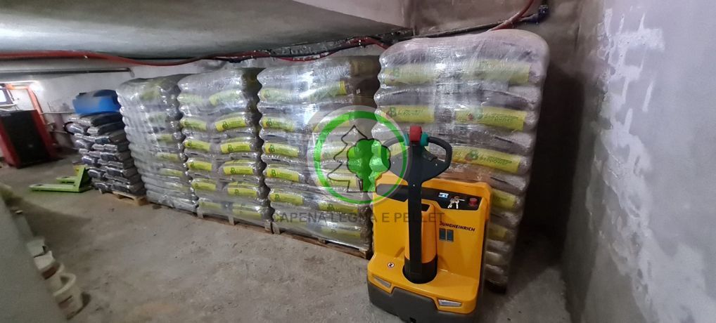 Un ambiente di magazzino con file di sacchi impilati e pallettizzati e un transpallet elettrico giallo parcheggiato in primo piano.