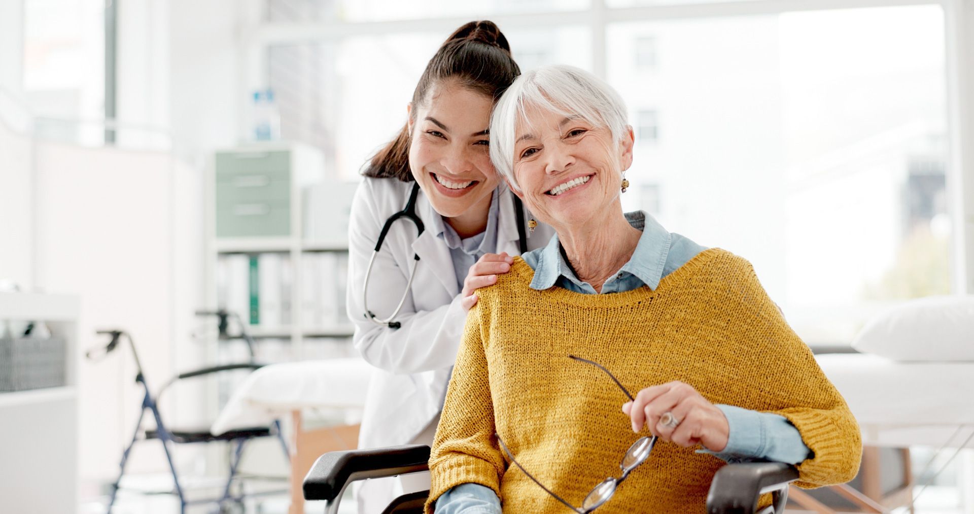 Smiling doctor with stethoscope and elderly woman in wheelchair.