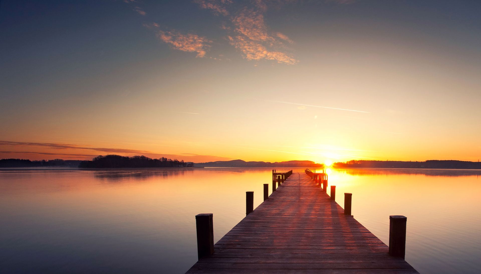 Wooden pier leading into a calm lake at sunrise, with golden light on the horizon. Wooden pier leading into a calm lake at sunrise, with golden light on the horizon.