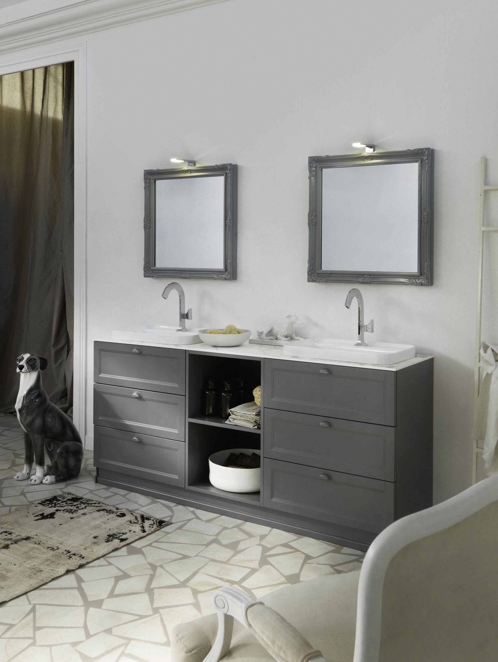 Bagno moderno con doppio lavabo grigio, due specchi, applique e pavimento piastrellato con motivi decorativi.