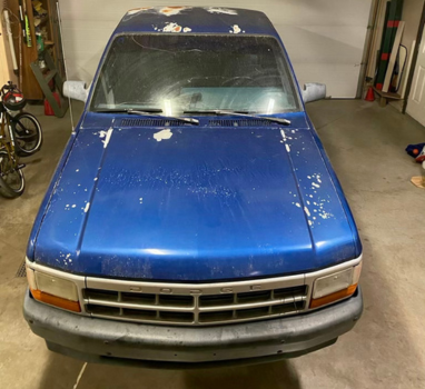 A blue truck is parked in a garage next to a garage door.