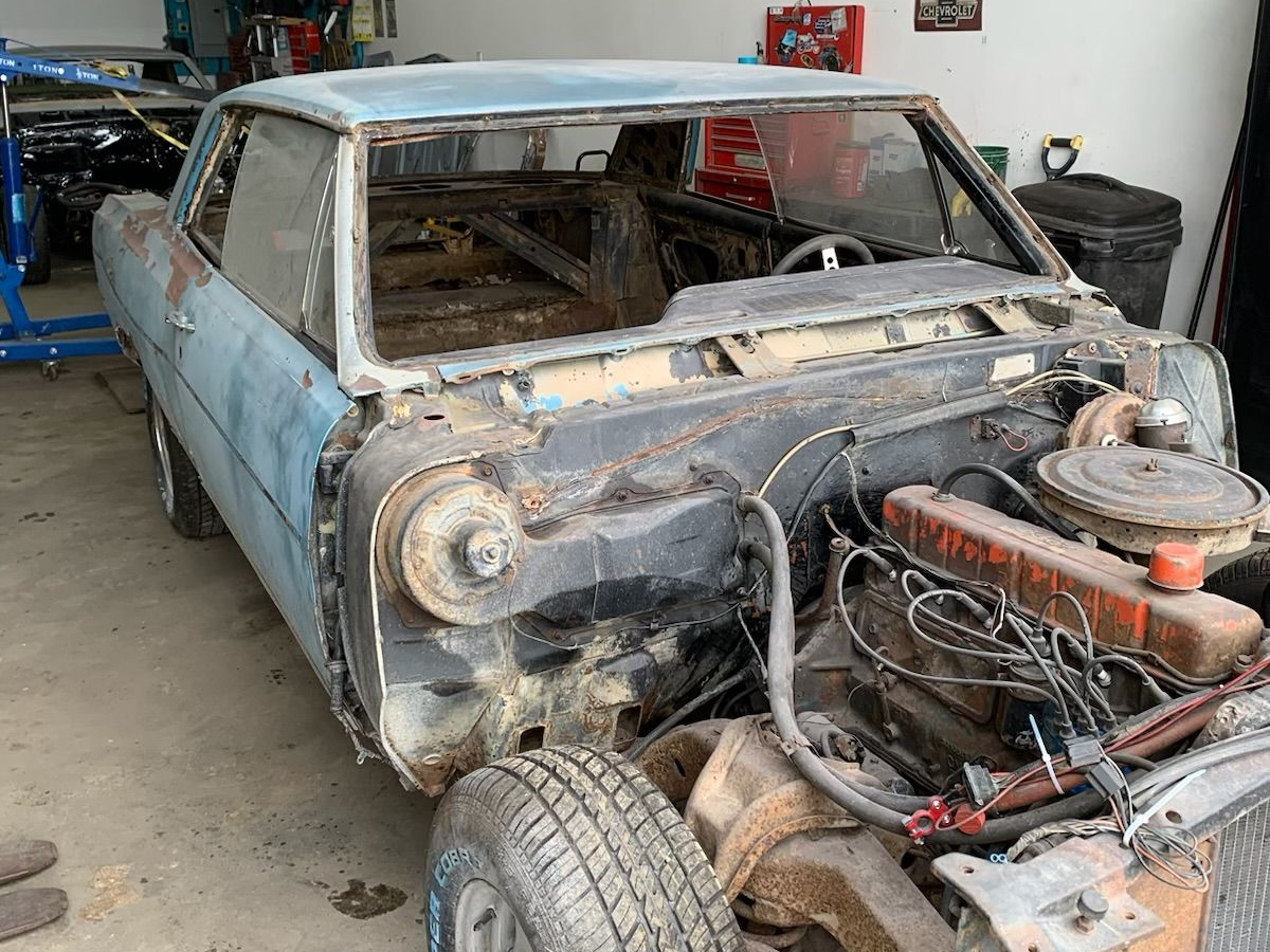 Rusty blue classic car shell with missing windshield and exposed engine in a garage