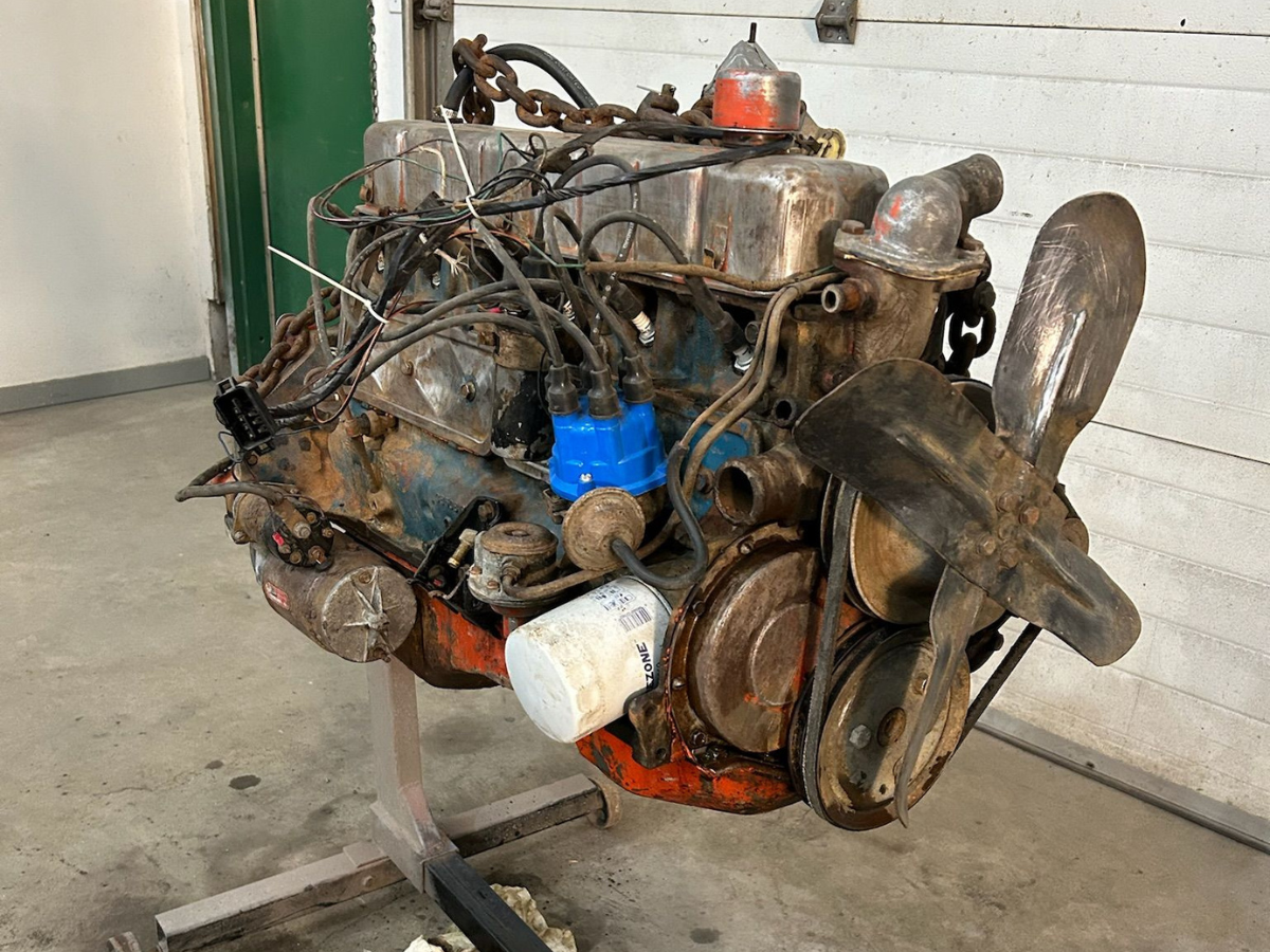 Old, partially disassembled engine with exposed wires and hoses on a metal stand in a workshop