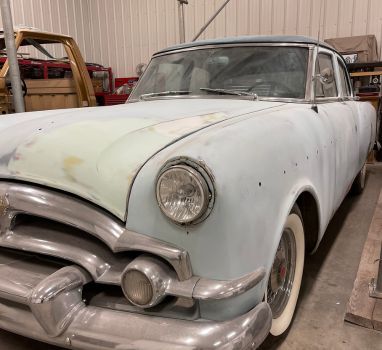 An old car is parked in a garage with white tires.
