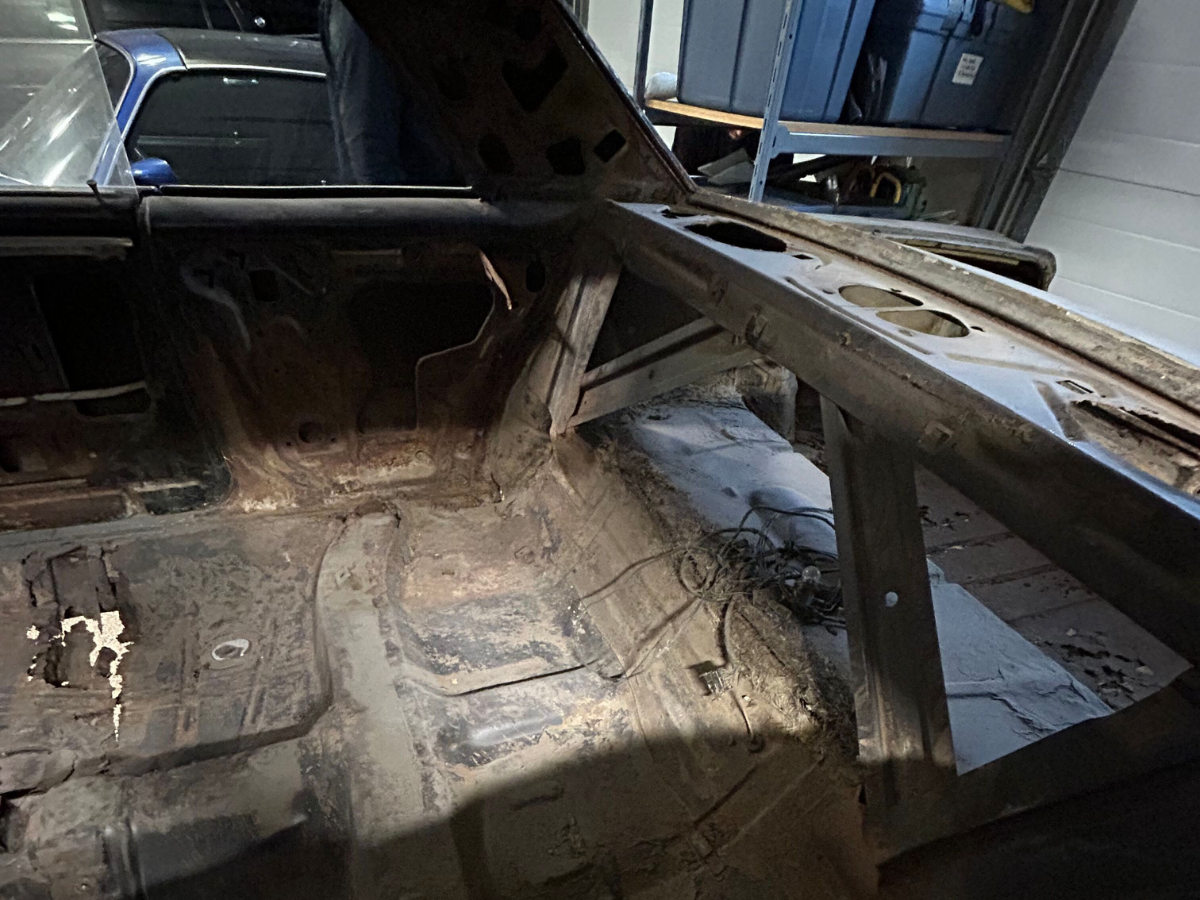 Interior of a stripped car shell with exposed metal and rust in a workshop or garage