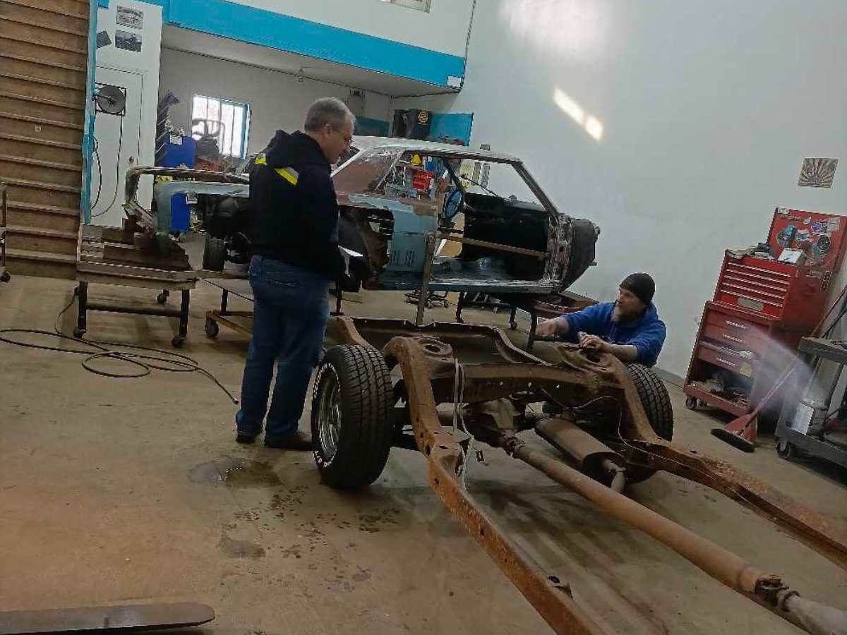 Auto workshop with a car chassis under repair and two mechanics working in a garage