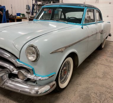 A light blue car with white tires is parked in a garage